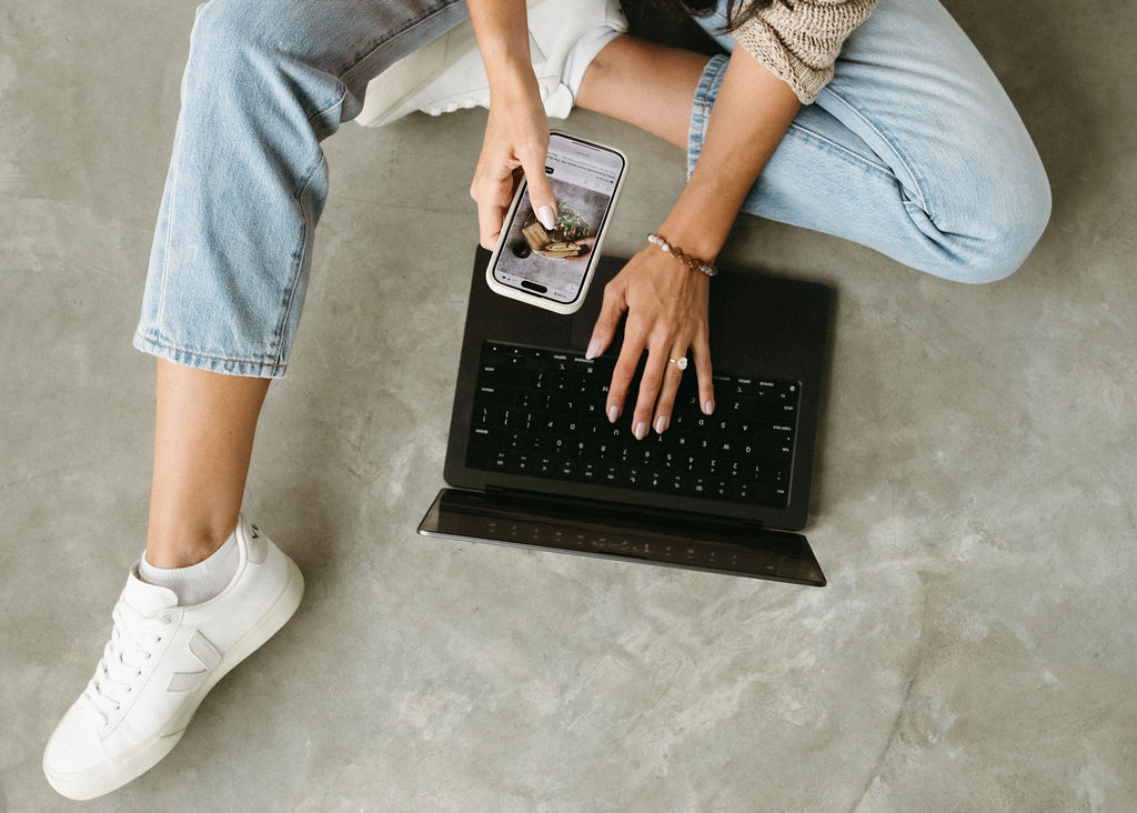 Calgary branding session with a woman holding her phone while typing on a laptop.